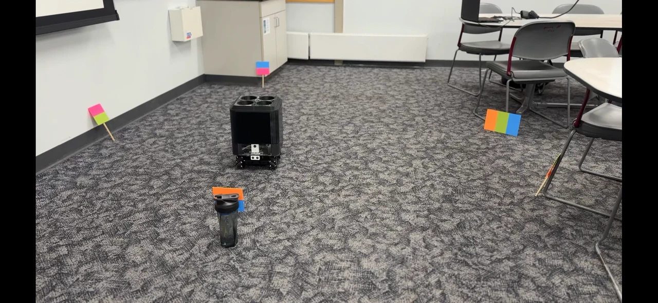 Delivery robot on a classroom floor among colored target cards, with a water bottle in the foreground.